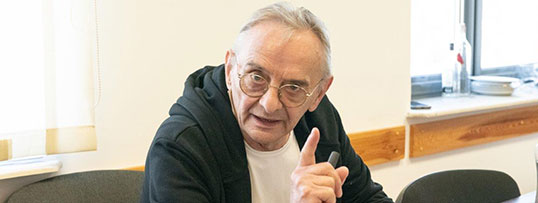 Twarz Jerzego Bończaka siedzącego za biurkiem. W dole zdjęcia widać fragment uniesionej przez niego dłoni z wyprostowanym palcem wskazującym
