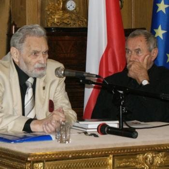 Bohdan Urbankowski siedzi za stołem przemawiając do stojącego na statywie mikrofonu. Z jego sprawej strony również za stołem siedzi patrząc na niego Marek Mokrowiecki.