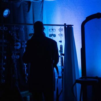 Szymon Cempura w ciemności na tle wystawy okularów i lustra