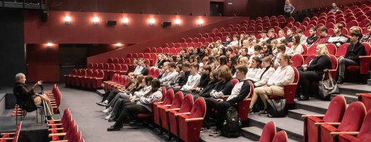 Młodzież siedząca na widowni Dużej Sali, na scenie dyrektor Marek Mokrowiecki