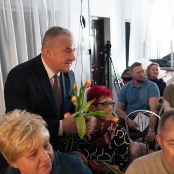 Lech Dąbrowski rozdaje siedzącym na scenie paniom kwiaty