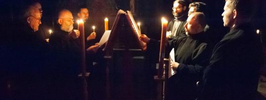 Mężczyźni ze świecami w dłoniach stoją wokół księgi